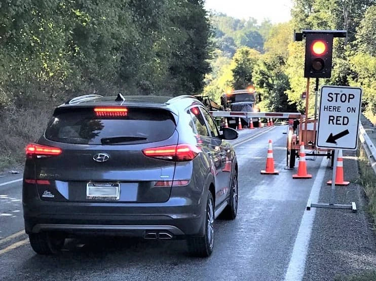A SUV is stopped at an automated flagger device that has a stop sign, a traffic signal, an automated gate to block the flow of traffic and traffic cones. 